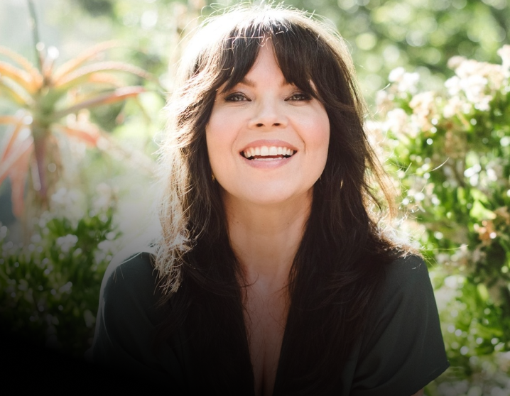 Danielle LaPorte smiling at the camera outside with flowers behind her.