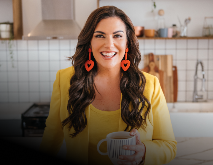 Amy Porterfield smiling in a yellow top holding a cup of coffee.