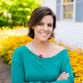 Colleen Kessler posing in front of a garden smiling with arms crossed.